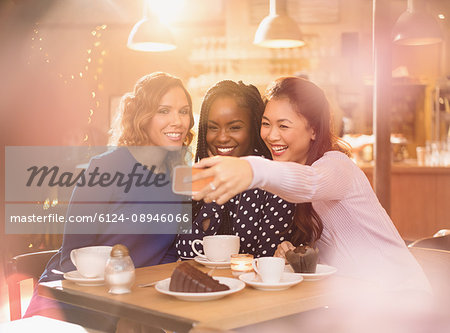 Smiling women friends taking selfie with camera phone at cafe table
