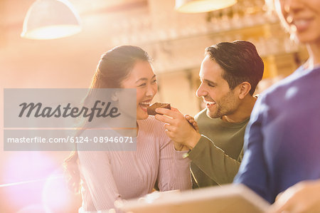 Playful boyfriend feeding brownie to girlfriend at cafe