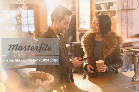 Couple with cell phone and coffee at counter in cafe