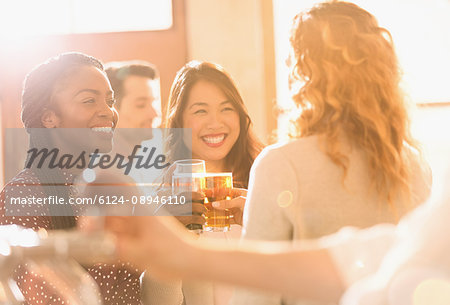 Smiling women friends toasting beer glasses in sunny bar