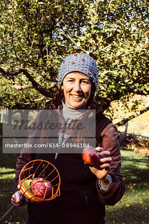 Portrait of woman holding fruit picker and fresh apple