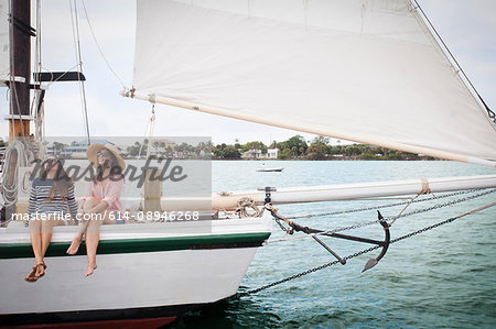 Two women on sitting on edge of sailing boat, legs dangling over the edge