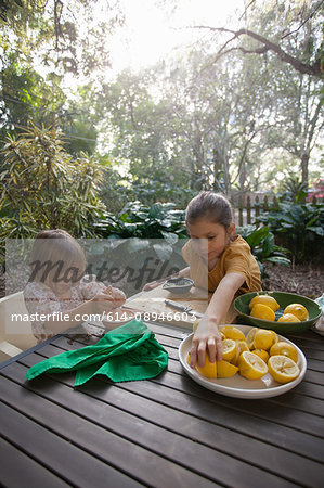 Two young sisters preparing lemons for lemonade at garden table