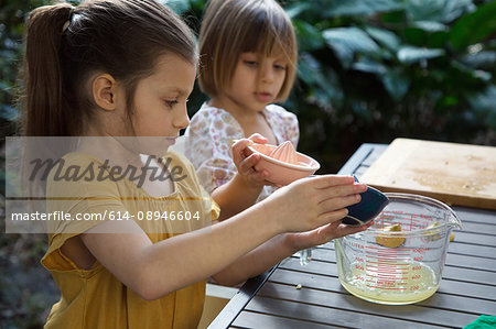 Two young sisters pouring lemon juice for lemonade at garden table