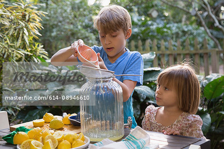 Boy and young sister pouring lemon juice for lemonade at garden table