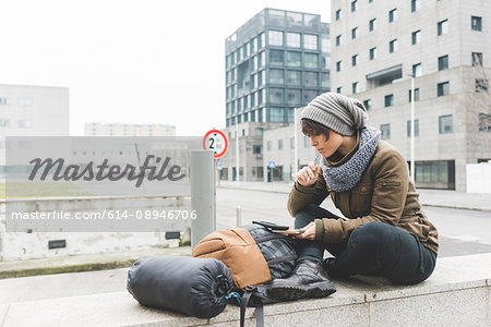 Female backpacker sitting on wall looking at notebook
