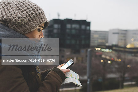 Woman in knit hat looking at smartphone in city at dusk