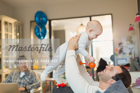 Male gay parents playing with baby son in living room