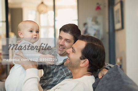 Male gay parents holding cute baby son on sofa