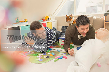 Male gay parents playing with baby son in playroom