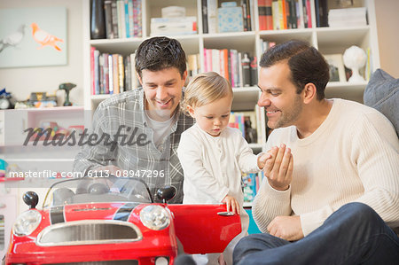 Male gay parents and baby son playing with toy car
