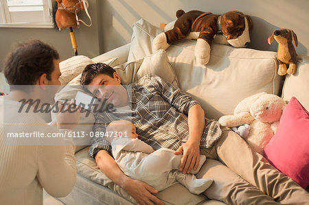 Male gay parents and baby son resting on living room sofa Male gay parents and baby son resting on living room sofa