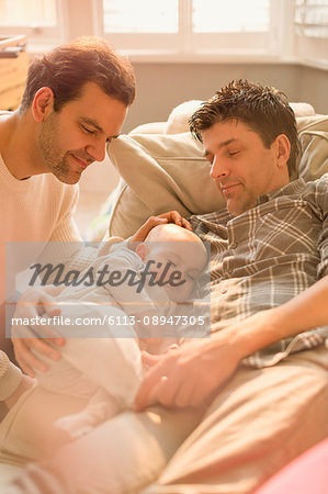 Male gay parents watching baby son sleeping on sofa Male gay parents watching baby son sleeping on sofa