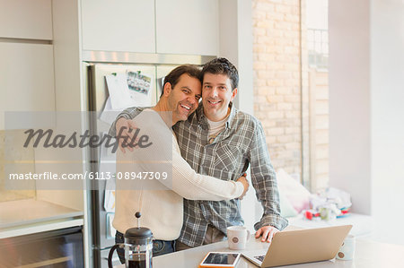 Portrait affectionate male gay couple hugging at laptop in kitchen