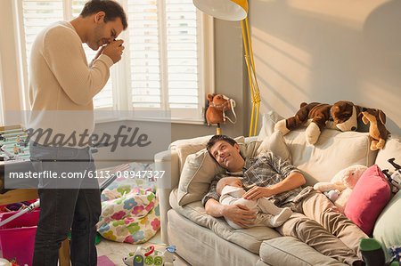 Male gay parents resting with baby son on sofa