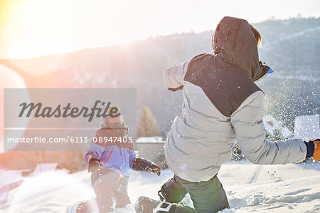 Playful couple enjoying snowball fight in sunny snowy field