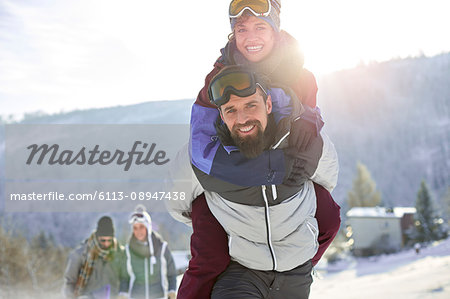 Portrait playful couple piggybacking in sunny, snowy field