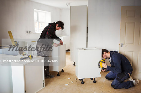 Two builders, building white kitchen units.