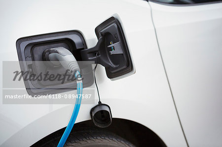 Close up of electric car being charged by a blue cable plugged in, topping up the battery.