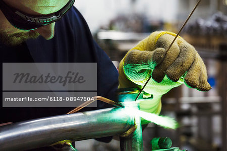 Male skilled factory worker using tools to weld and solder parts of a bicycle in a factory.