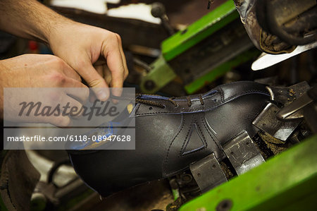 Close up of man standing in a shoemaker's workshop, tying the laces of a leather cycling shoe.