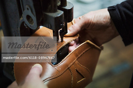 Close up of worker in a shoemaker's workshop, using a machine to punch holes into a leather shoe.