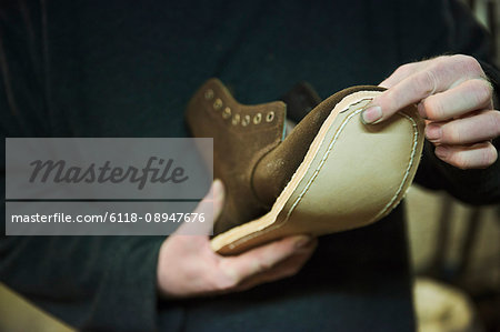 Close up of worker in a shoemaker's workshop, attaching a sole to a leather boot.