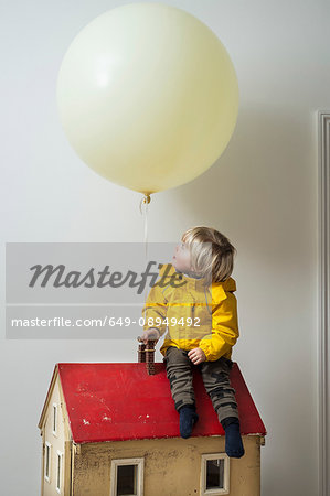 Boy sitting on dolls house looking up at balloon