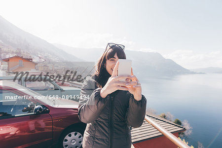 Mid adult woman taking smartphone selfie at lakeside, Monte San Primo, Italy