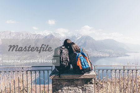 Rear view of couple sitting on terrace wall over mountain lakeside, Monte San Primo, Italy