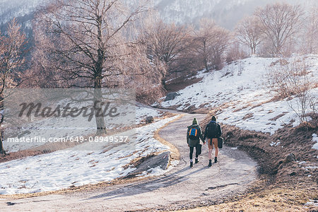 Rear view of hiking couple hiking along snowy rural road, Monte San Primo, Italy