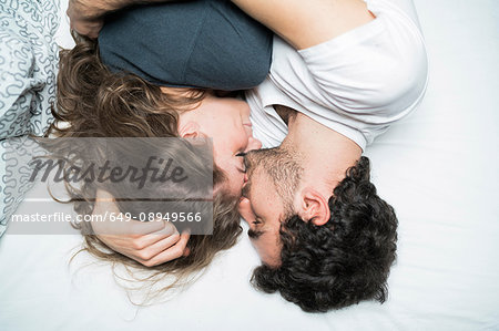 Overhead view of young couple lying in bed embracing