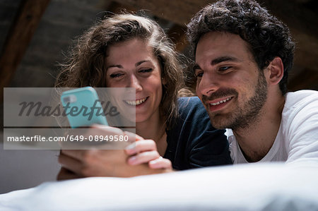 Young couple lying on bed looking at smartphone