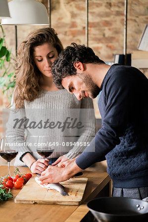 Young couple preparing fish at kitchen counter