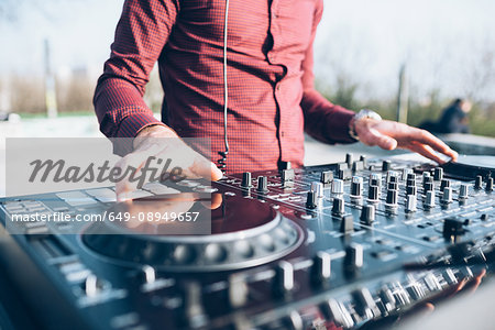 Young man using mixing desk at roof party, mid section, close-up