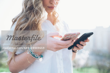 Young woman outdoors, looking at two smartphones, mid section