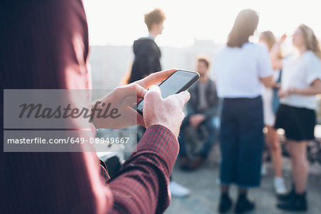 Group of friends enjoying roof party, young man using smartphone