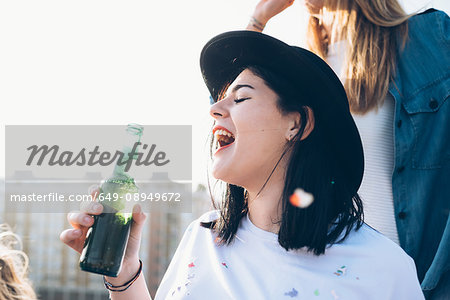 Group of friends enjoying roof party, young woman holding beer bottle