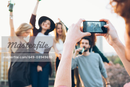 Group of friends enjoying roof party, young man taking photograph using smartphone