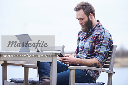 Young male designer looking at smartphone on waterfront outside design studio