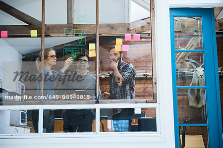 Design team writing on adhesive notes and drawing on design studio window