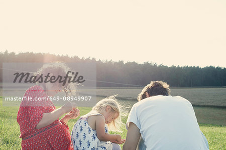 Couple sitting in field with toddler daughter looking at grasses