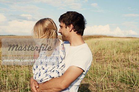 Mature man carrying toddler daughter looking out from wheat field