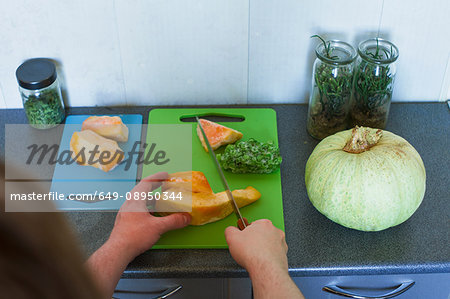 Over shoulder view of male hands chopping pumpkin on cutting board