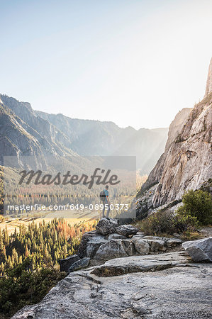 Man on boulder looking out at valley forest, Yosemite National Park, California, USA