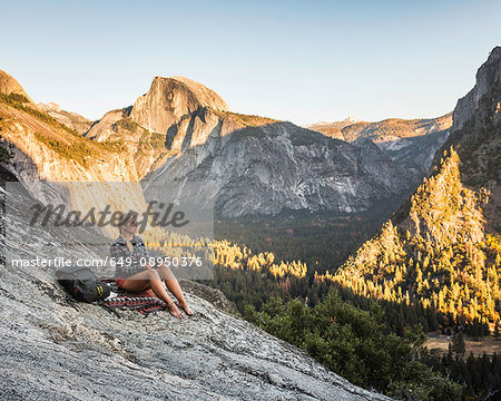 Woman on rock looking out at valley forest, Yosemite National Park, California, USA