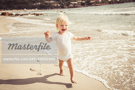 Young boy walking along beach, smiling