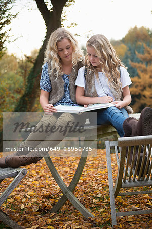 Portrait of two sisters sitting on patio table reading book in autumn garden
