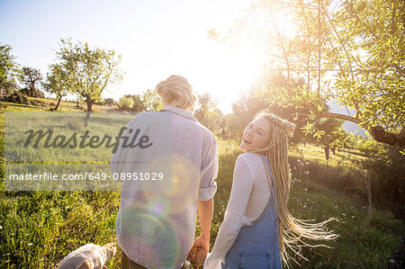 Rear view of young couple walking dog in sunlit rural field, Majorca, Spain