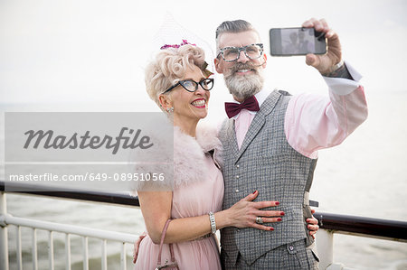 1950's vintage style couple taking smartphone selfie on pier
